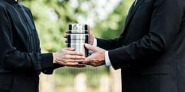2 Menschen übergeben sich eine Urne aus Metall