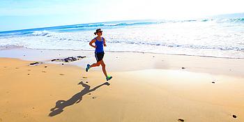 Eine junge, sportliche Frau, die am Strand entlangjoggt 