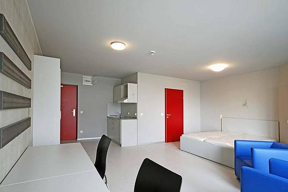 Zimmer mit schlichter weißer Einrichtung, 2 rote Türen, 2 schwarze Stühle, 2 blaue Fauteuils