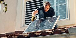 Das Bild zeigt einen Arbeiter auf einem Dach, der ein Solarpaneel montiert.