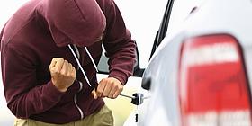 Person mit weinroter Kaputzenjacke versucht ein Autotür mit einem Schraubenzieher zu öffnen