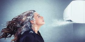 Frau steht vor Klimagerät und hat Frost in den Haaren