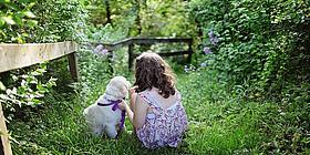 Kind mit einem kleinen Hund sitzt in einem grünen Garten