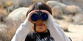 Das Bild zeigt ein Kind, das durch ein Fernglas schaut. 
