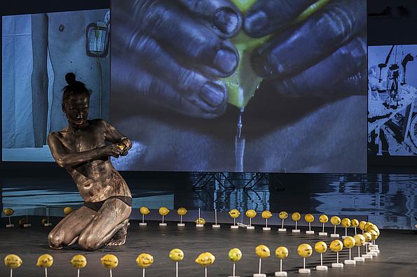 Performance beim ImPulsTanz Festival: Frau schwarz angemalt inmitten von aufgespießten Zitronen. 