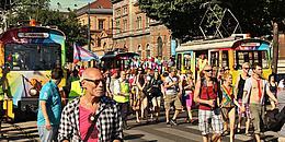 Bunte Straßenbahnen neben Menschenmassen auf der Regenbogenparade