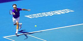 Ein Tennisspielen mit Schläger in der Hand rennt auf blauem Boden