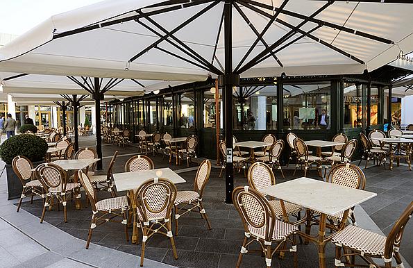 Tische und Sessel unter Schirmen vor einem Café im Designer Outlet Parndorf