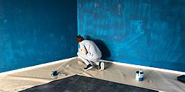 Frau hockt am Boden vor blauer gefleckten Wand und streicht sie