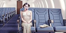 Animation mit Frau im Flugzeug auf einem Sitzplatz, die mit dem rechten Auge zwinkert. Auf dem Nachbarsitz liegt ein aufgeschlagenes Buch.