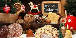 Ein schön angerichteter Weihnachtstisch mit Lebkuchen,Tannenzweigen und zapfen,Kerzen und Christbaumschmuck.Im Hintergrund eine kleine Tafel mit dem Gruß Frohe Weihnachten!