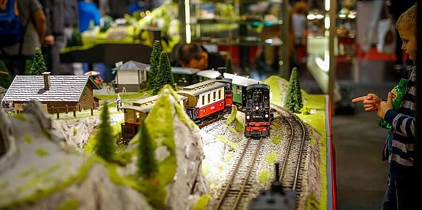 eisenbahn Modell daneben ein Kind das auf eine Lokomotive zeigt