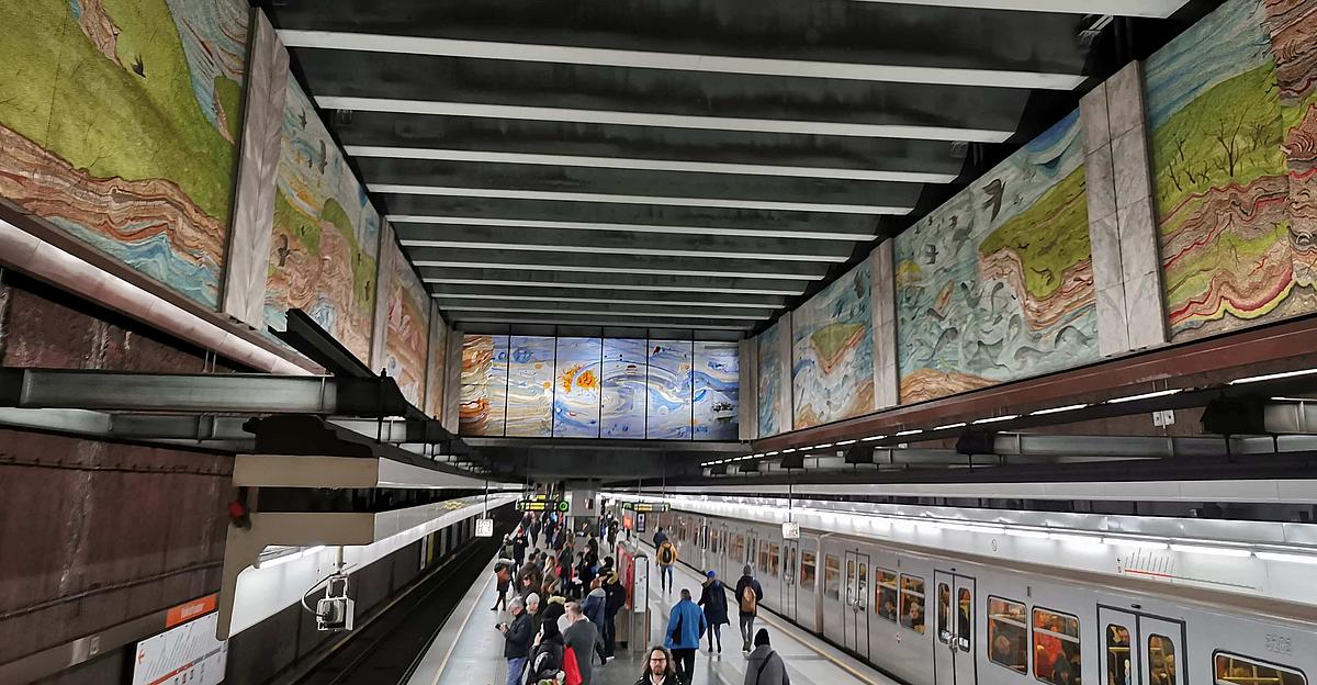 In einer U-Bahn Station ist ein riesiges buntes Mosaik über drei Wände verteilt und über den Gleisen angebracht