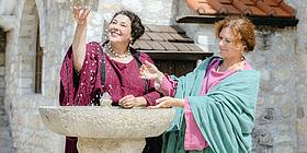 Zwei Frauen in traditionell römischen Gewändern an einem Springbrunnen