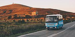 Das Bild zeigt einen kleinen Reisebus mit einem Hügel im Hintergrund.