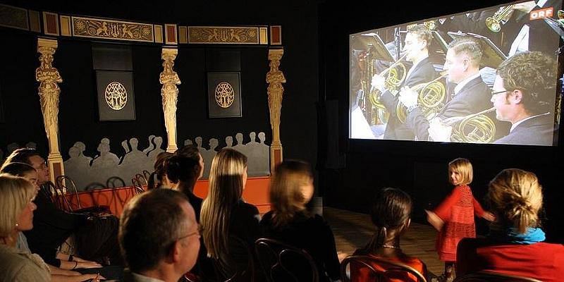 Imaginärer Konzertsaal im Klangmuseum Wien mit Besuchern, die vor einer Leinwand sitzen