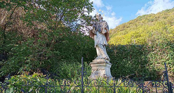 Eine Statue steht vor einem Gebüsch und hinter einem Metalzaun von Gräsern umgeben