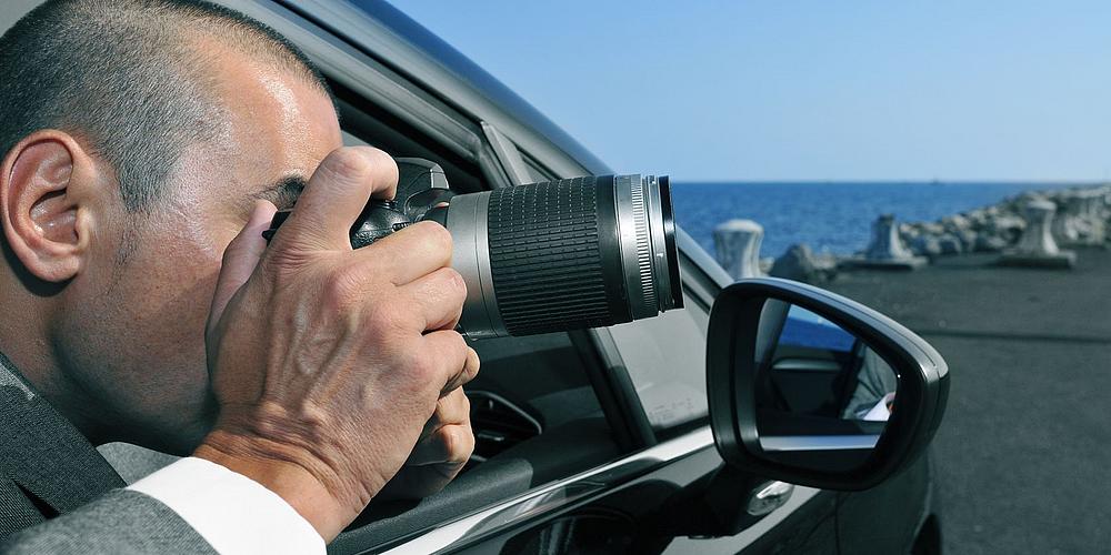 Mann mit Teleobjektiv und Kamera im Auto