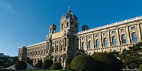 Frontalansicht des Gebäudes Naturhistorisches Museum Wien mit grünem Garten im Vordergrund und bei strahlendem Sonnenschein.