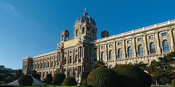 Frontalansicht des Gebäudes Naturhistorisches Museum Wien mit grünem Garten im Vordergrund und bei strahlendem Sonnenschein.