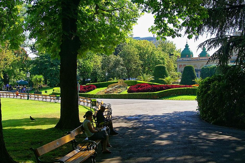 Eingang zum Stadtpark Wien mit Sitzbänken, im Hintergrund die Blumenuhr