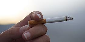 Angerauchte Zigarette, die eine Person zwischen ihrem Zeige- und Mittelfinger hält