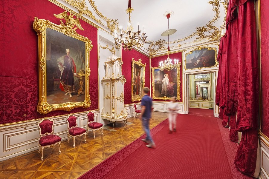 rotstrahlender Damast an den Wänden und große Gemälde von alten Kaisern