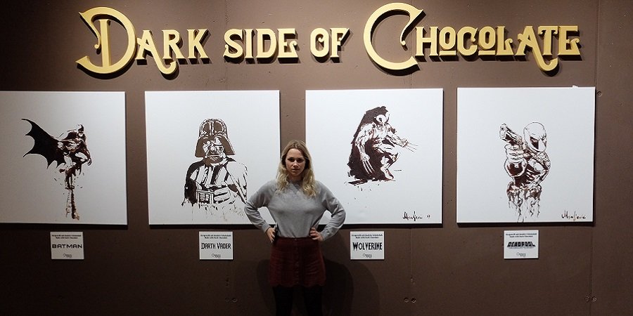 "The Dark Side of Chocolate"-Schriftzug auf Brauner Wand mit vier Bildern, Dame mit grimmigem Blick