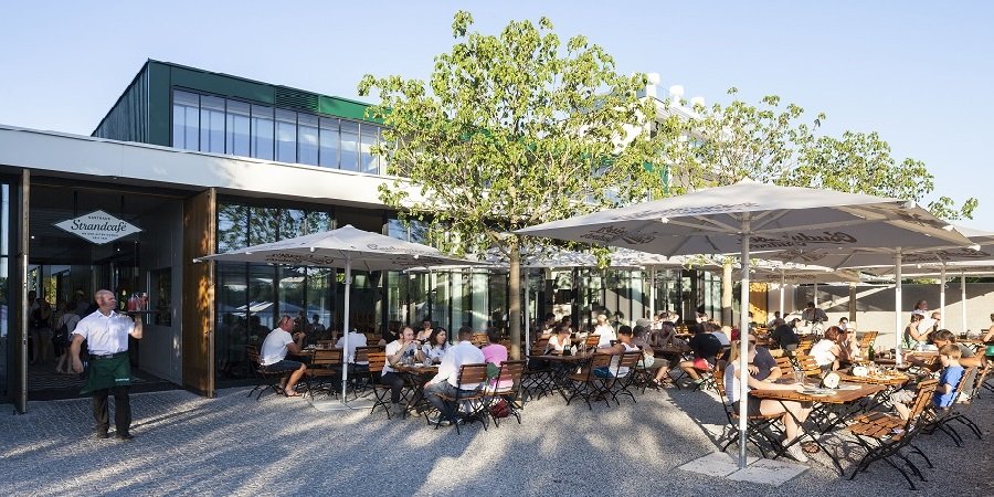 Restaurant mit Menschen die unter weißen Sonnenschirmen sitzen