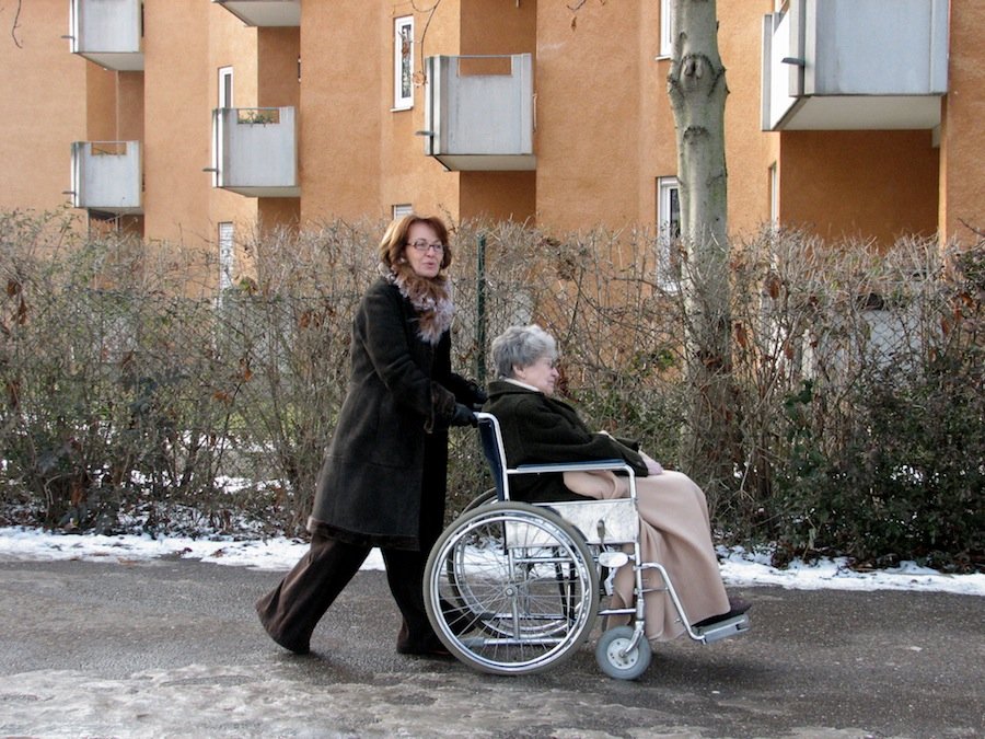 Frau schiebt ältere Frau mit dem Rollstuhl.