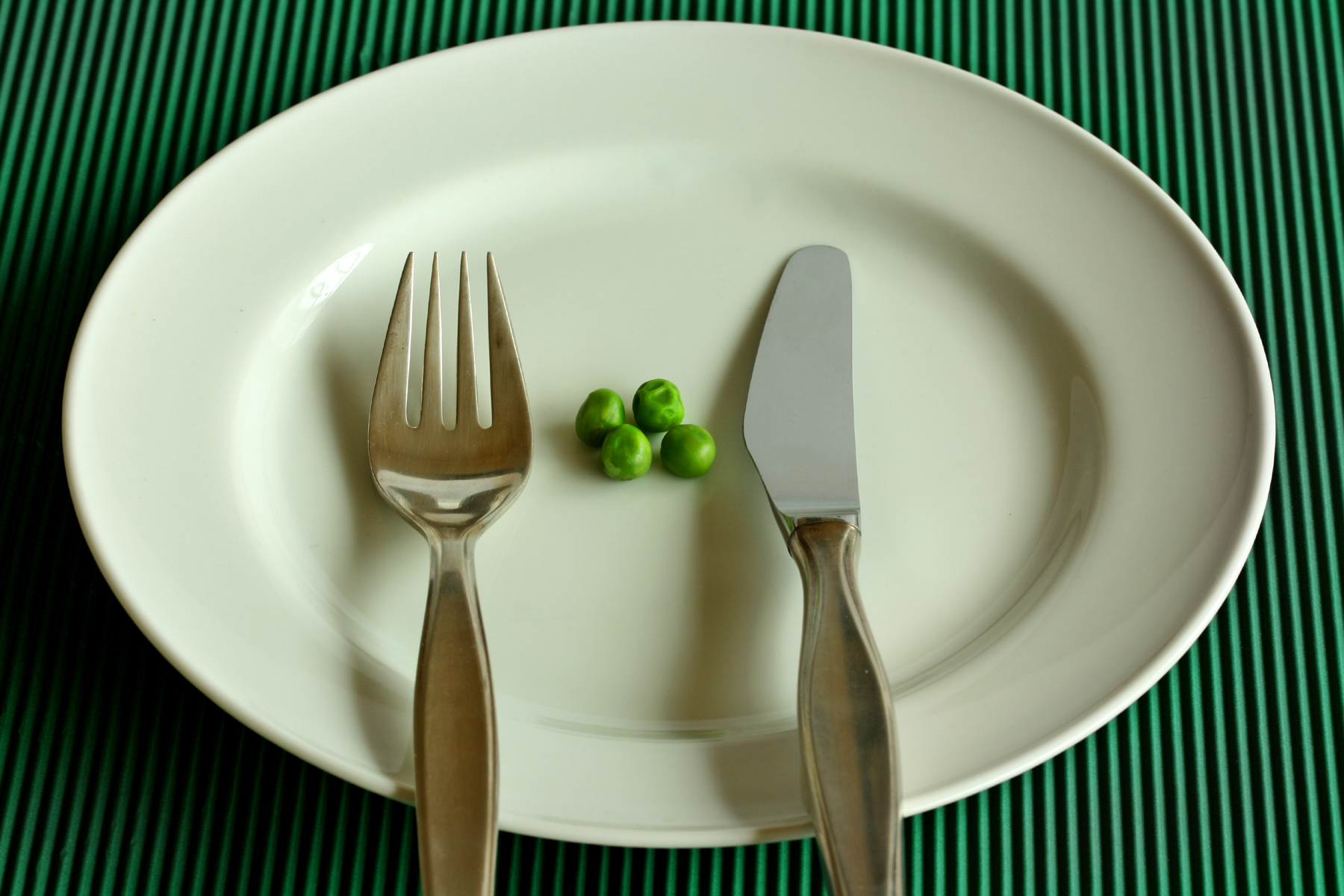 Erbsen und Gabel und Messer auf einem weißen Teller vor grünem Hintergrund