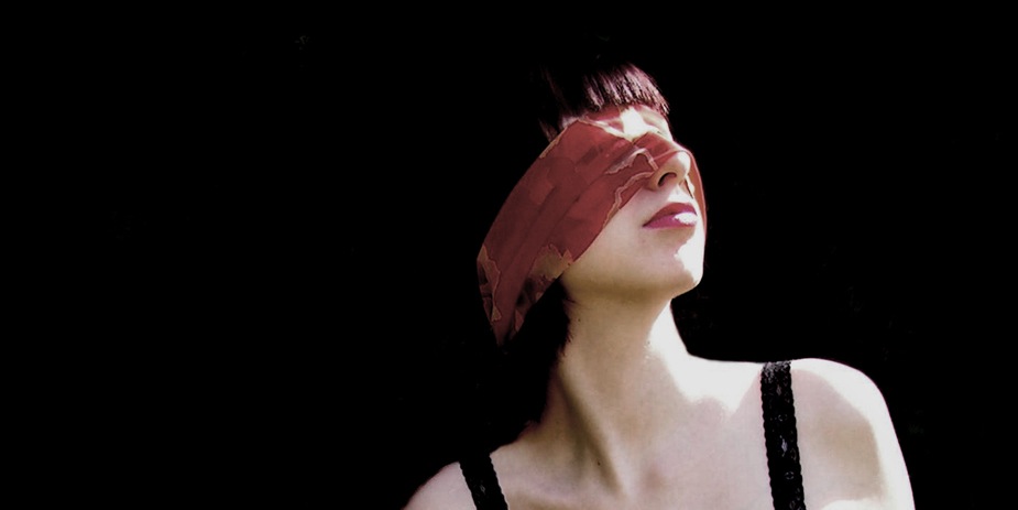 Eine rote Augenbinde tragende Frau vor schwarzem Hintergrund