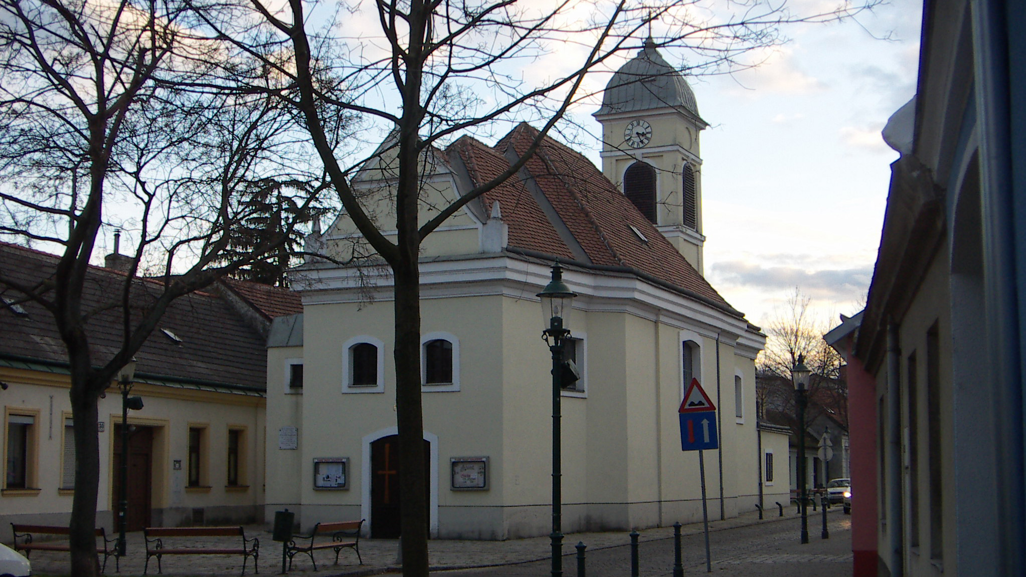 Bild von Kirche in Groß-Jedlersdorf und ihrem Vorplatz, auf dem ein paar Parkbänke stehen.