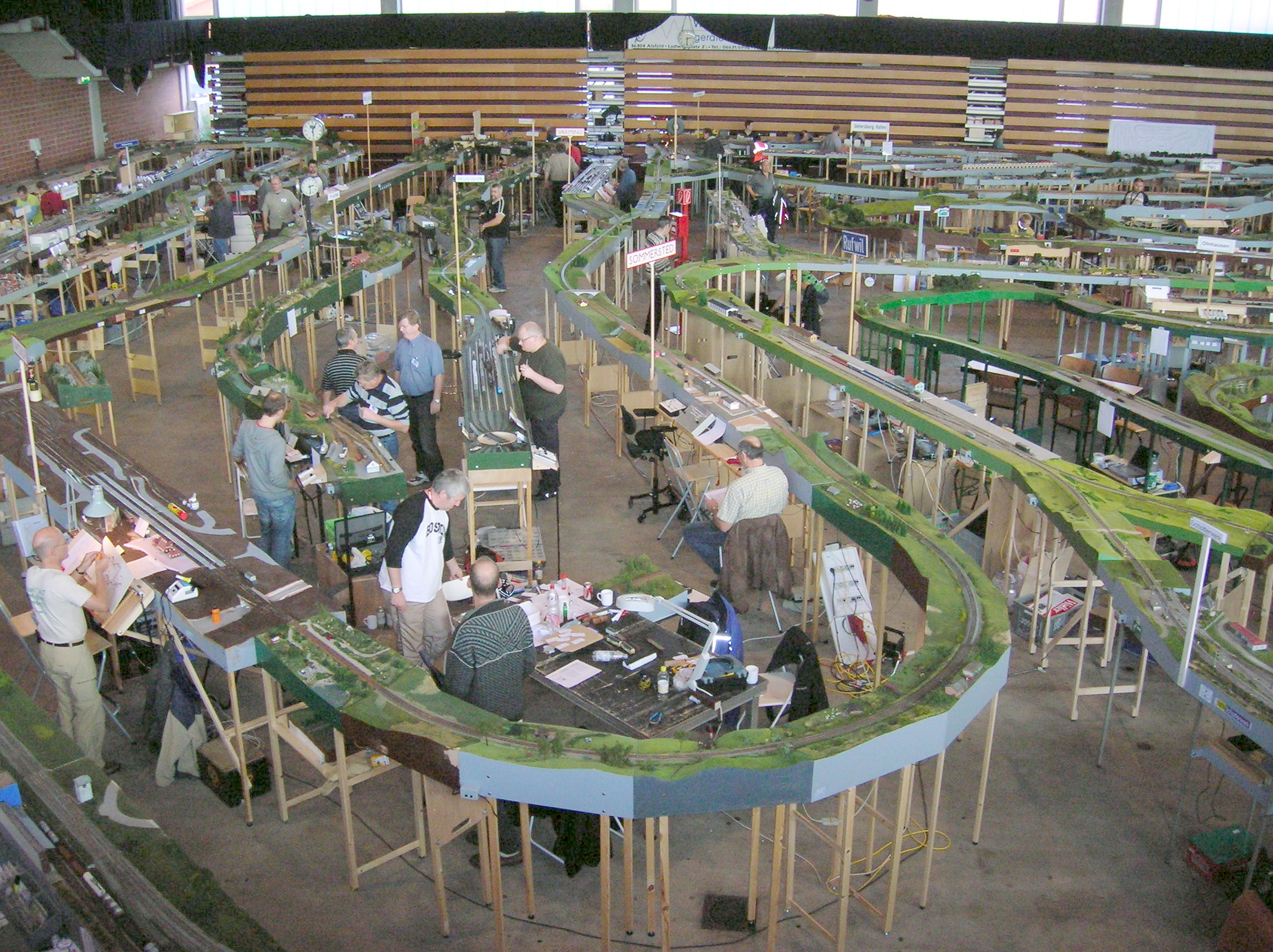 Ein riesige Modelleisenbahn wurde von mehreren Menschen in einer Halle aufgebaut.