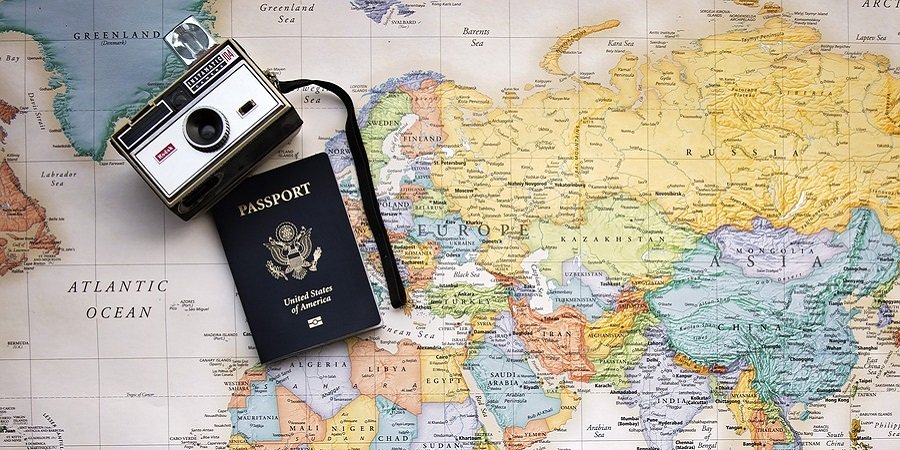 eine Weltkarte ist zu sehen, darüber ein blauer Reisepass und eine Kamera 