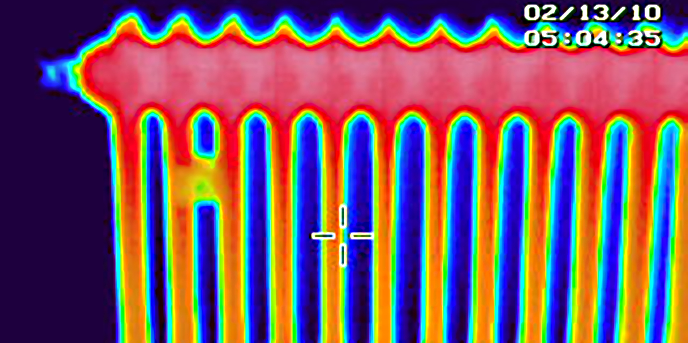 Infrarot-Wärmebild eines Zentraheizungskörpers. Dunkelblauer Hintergrund, die Zentralheizung ist oben rot, nach untengehend wird die Heizung gelb