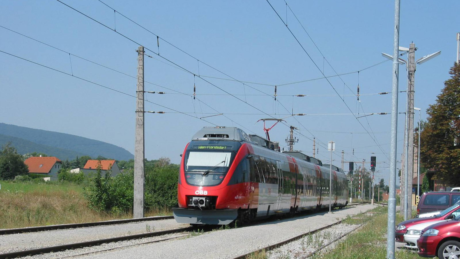 S Bahn-Linie S7 fährt Richtung Floridsdorf, über Flughafen Wien Schwechat. Neben den Gleisen befinden sich Parkplätze.