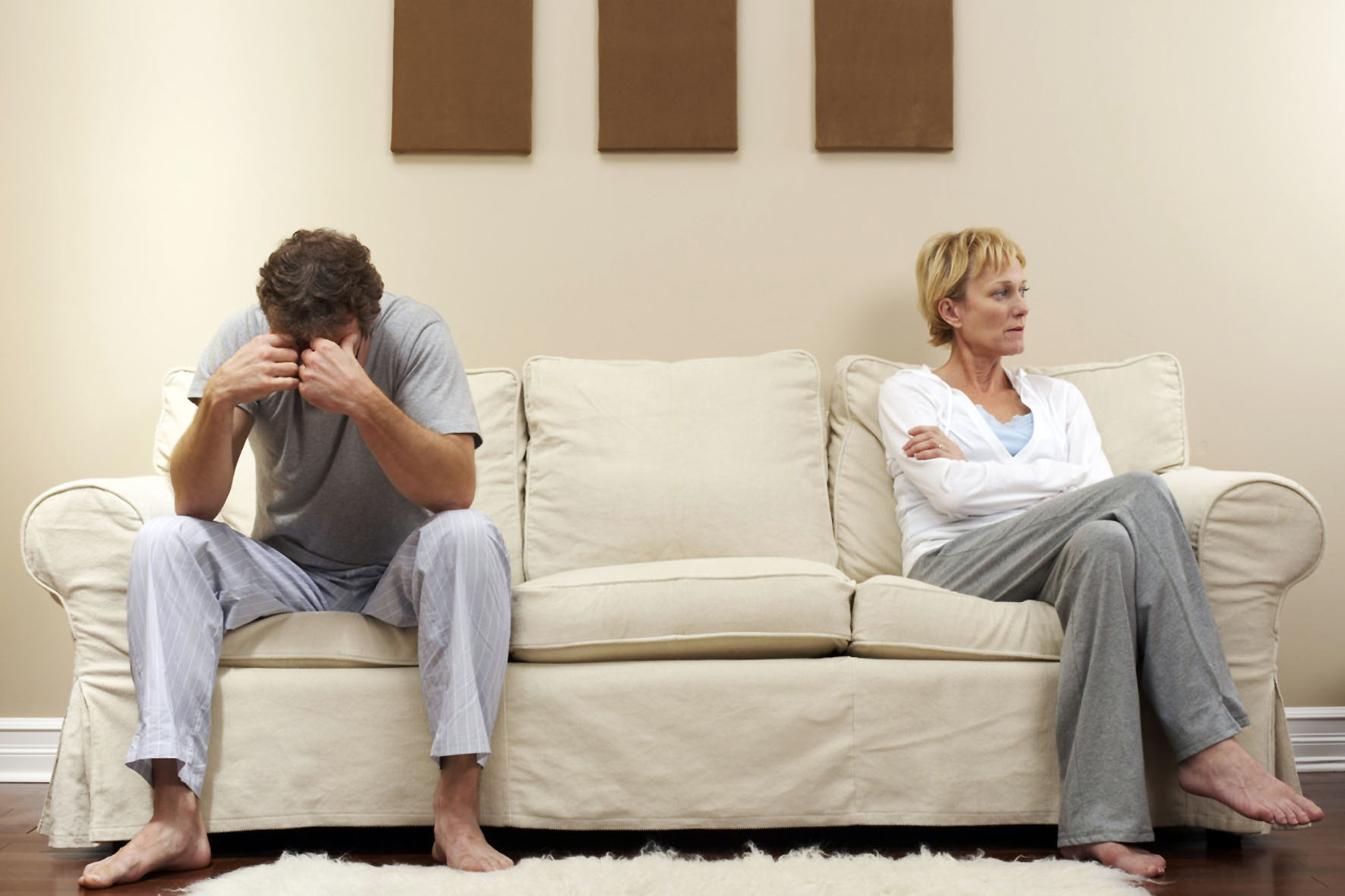 Mann und Frau an je einem Ende einer weißen Couch und voneinander abgewandt 