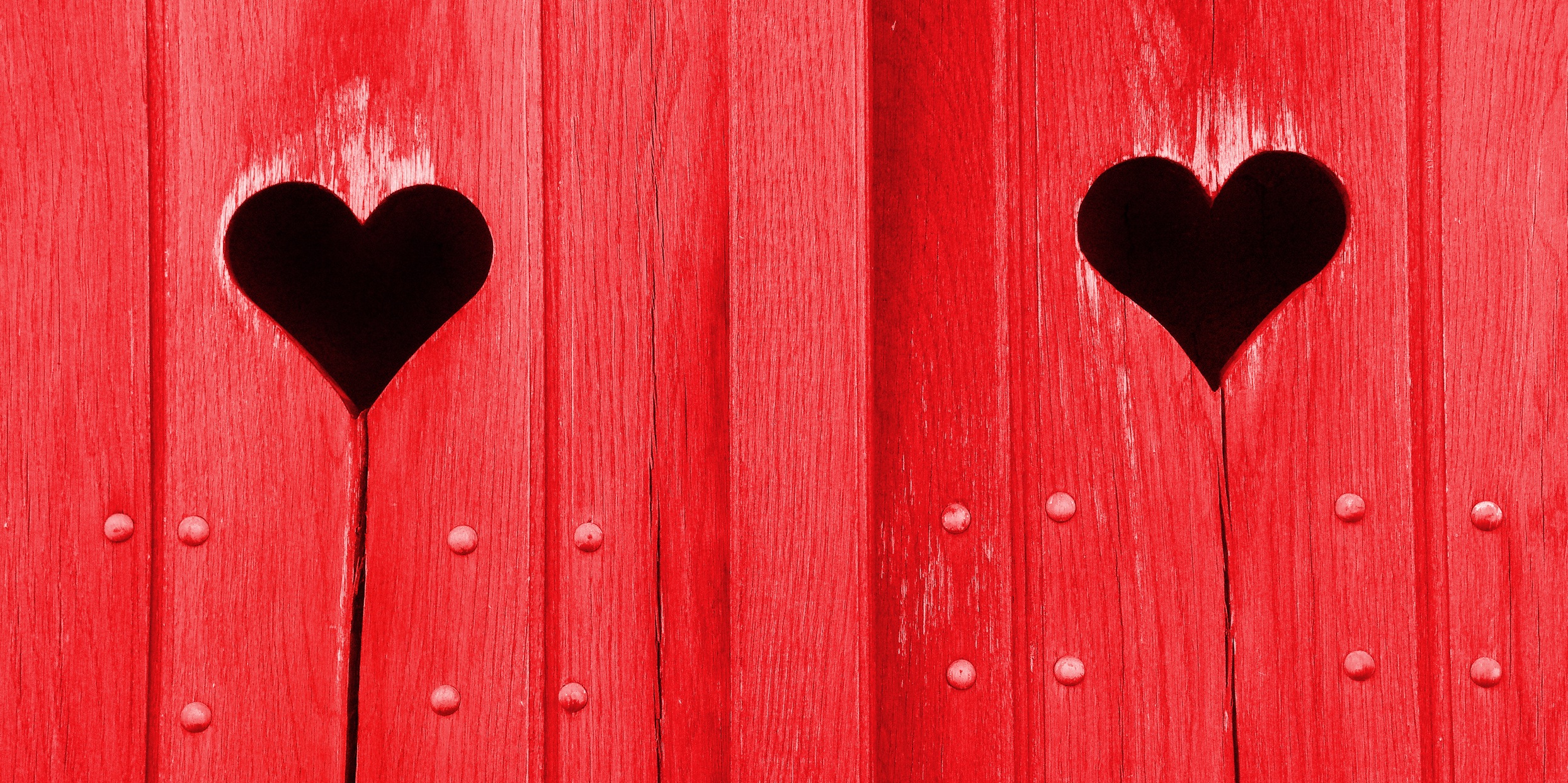 Zwei Löcher in Herzform in rot gestrichenen Fensterläden 