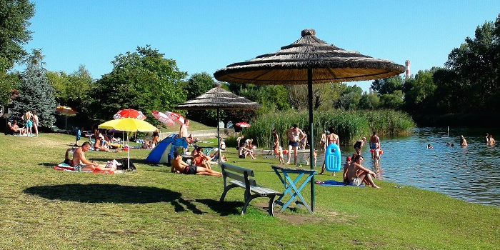 Menschen sonnen sich auf der Wiese und baden im Strandbad Stadlau. 