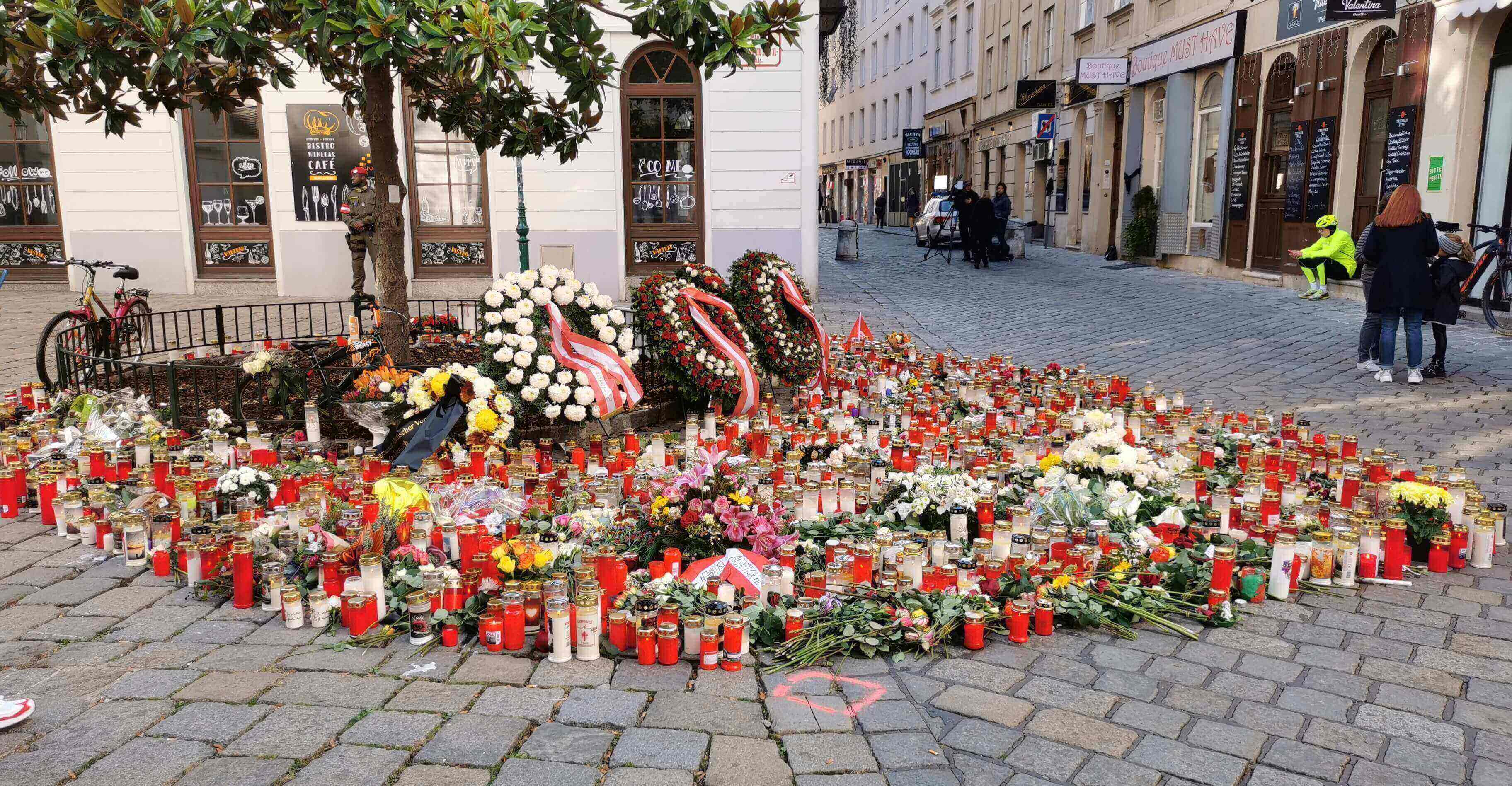 Ein Meer von Kerzen und Blumen ist herzförmig vor drei Kränzen, die neben einem Baum lehnen, aufgestellt worden.