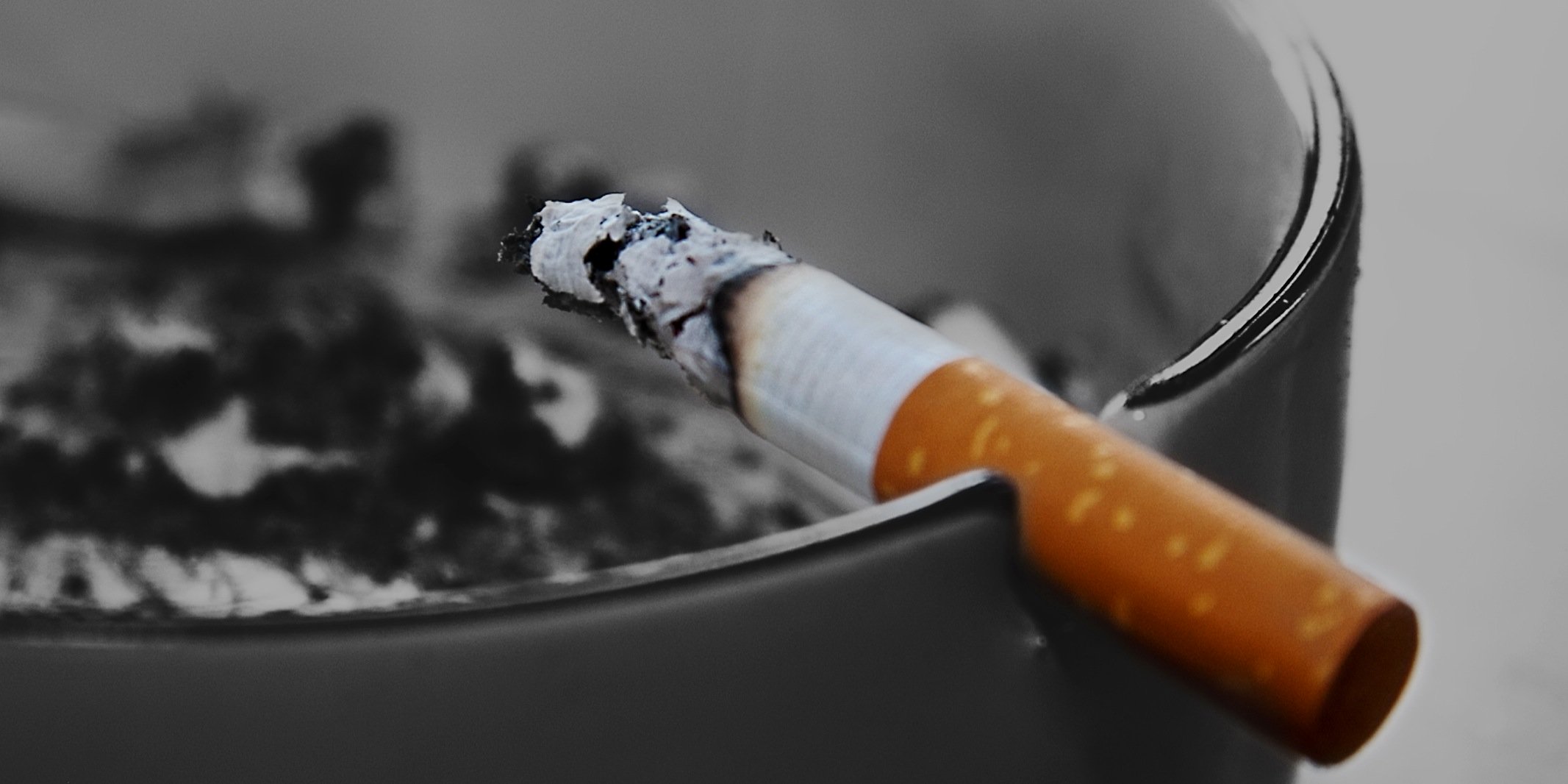 Eine halb gerauchte Zigarette am Rande eines Aschenbechers 