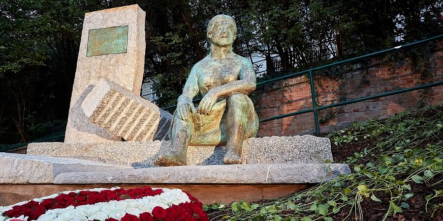 Grünes Denkmal zeigt eine Frau davor rote und weiße Rosen