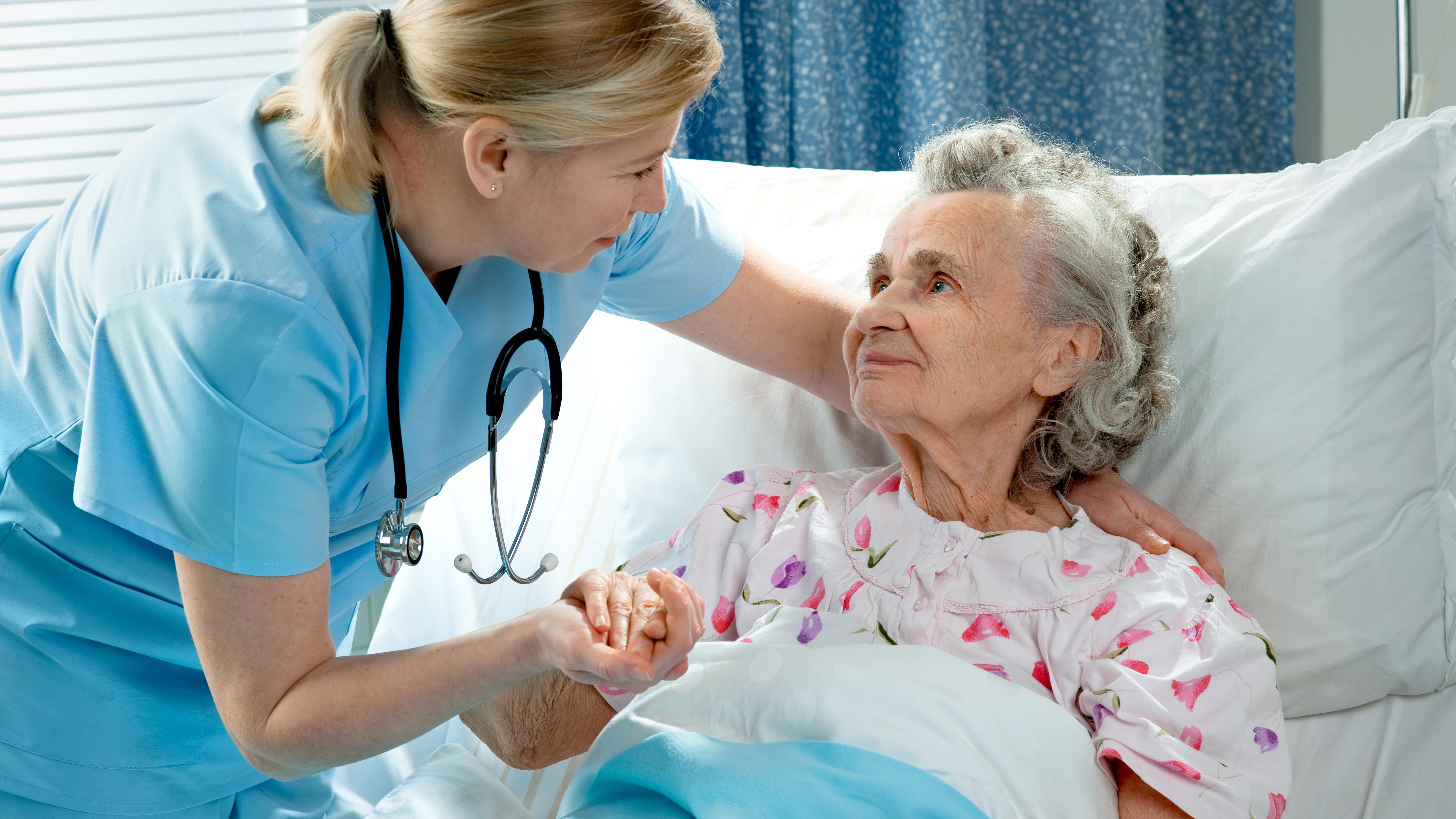 Pflegerin kümmert sich um alte Frau, die im Bett liegt.