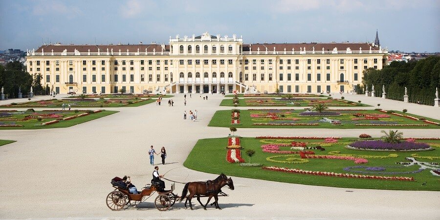 Fiaker fährt an Schloss Schönbrunn und der säuberlich gepflegten Gartenanlage vorbei.