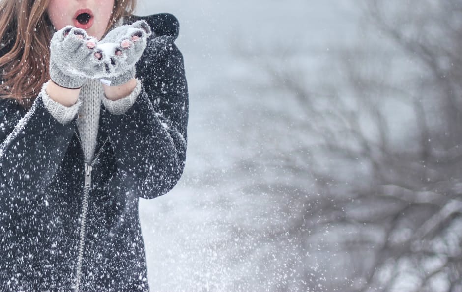 Frau pustet Schnee aus Händen mit Handschuhen überzogen