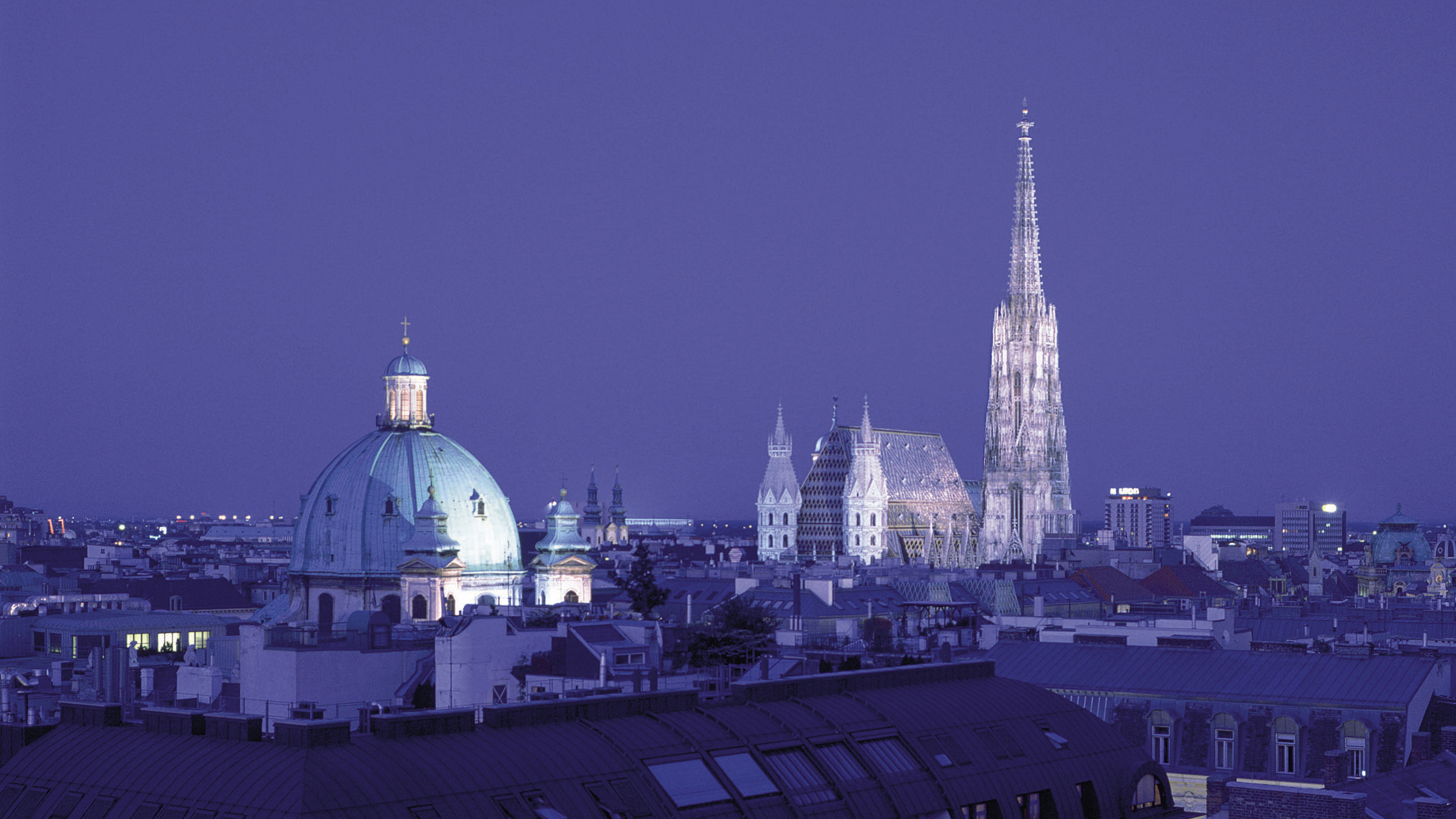 Nachtaufnahme von der beleuchteten Peterskirche und dem Stephansdom.