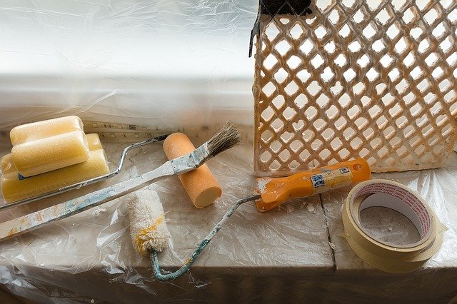 Schwamm, zwei Farbroller, Pinsel, Malerkrepp und Abstreifgitter auf Plastikfolie auf Fensterbrett