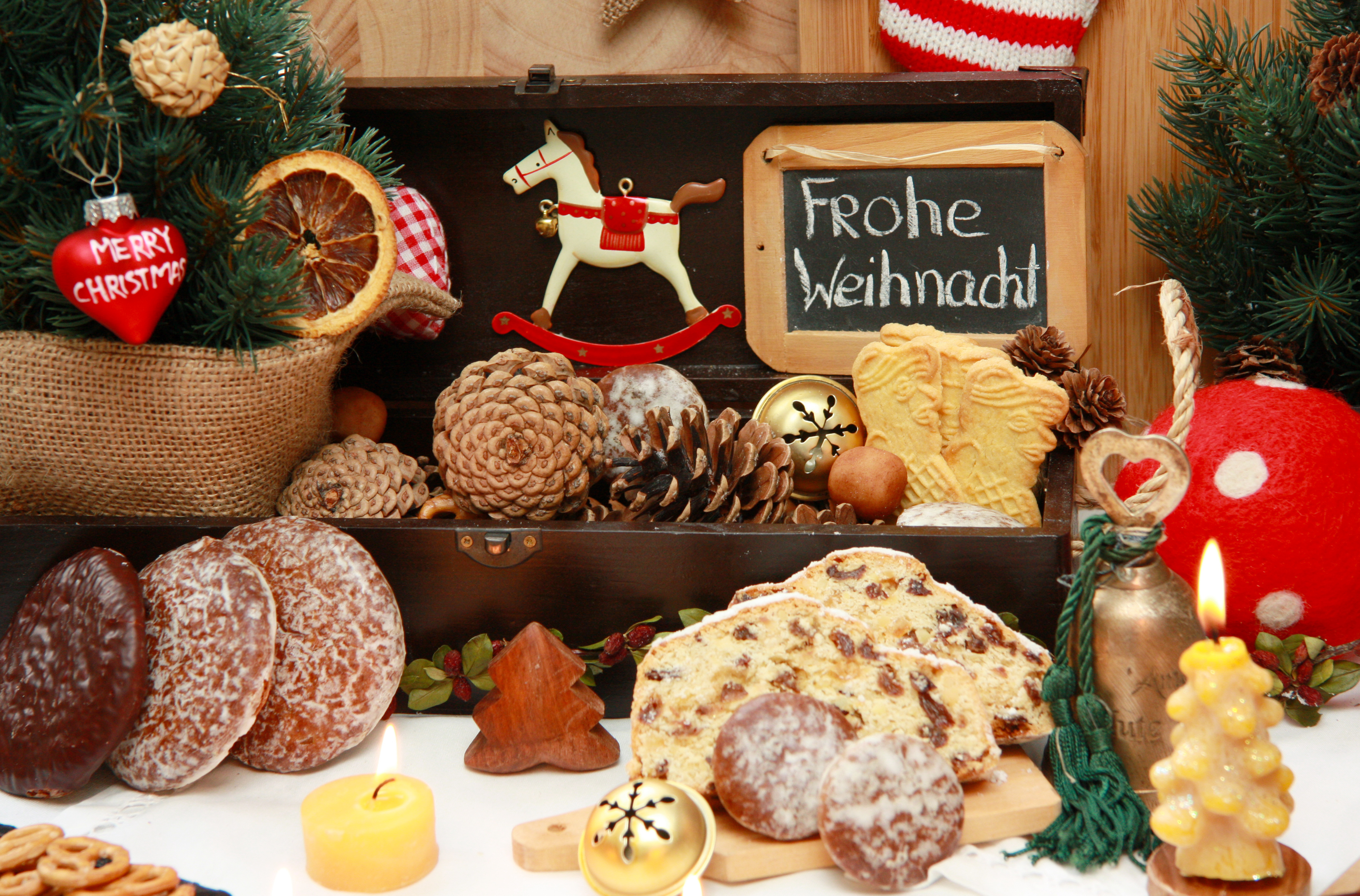 Ein schön angerichteter Weihnachtstisch mit Lebkuchen,Tannenzweigen und zapfen,Kerzen und Christbaumschmuck.Im Hintergrund eine kleine Tafel mit dem Gruß Frohe Weihnachten!