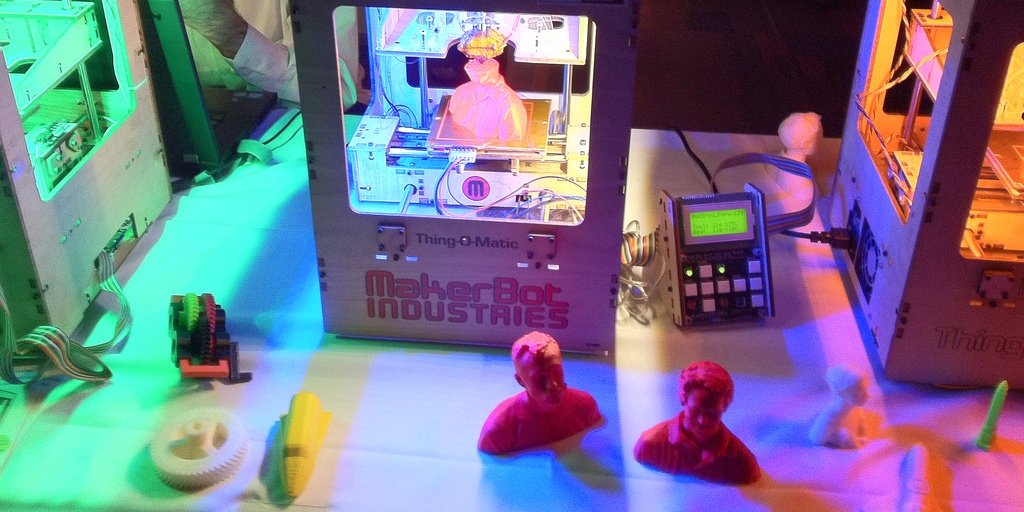 Ein 3D-Drucker und die damit erstellten Objekte - Büsten, Zahnräder und kleine Spielzeuge in verschiedenen Farben.